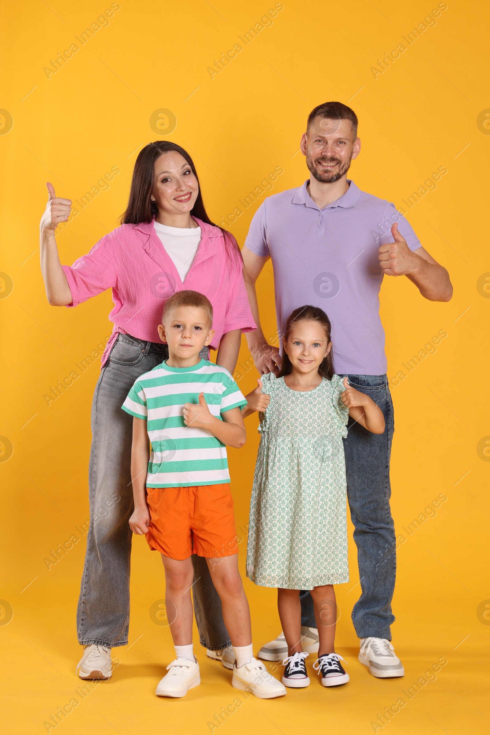 Photo of Happy family showing thumbs ups on yellow background
