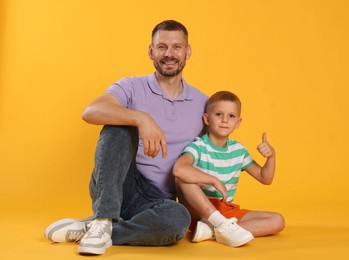 Photo of Happy father and son showing thumbs up on yellow background