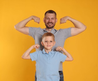 Photo of Father and son showing biceps on yellow background