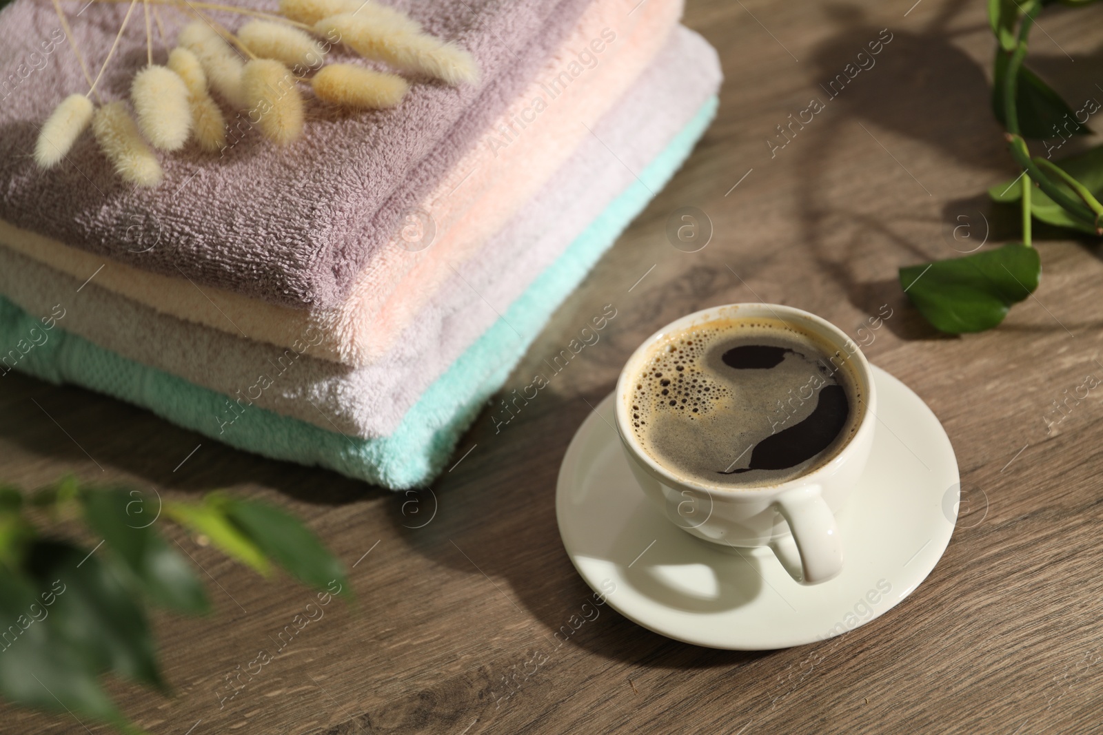 Photo of Stacked fresh terry towels and cup of coffee on wooden table indoors, closeup