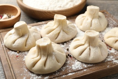 Photo of Uncooked khinkalis (dumplings) with peppercorns on wooden board, closeup