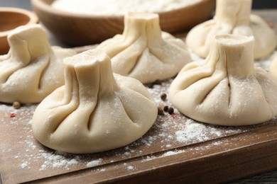 Photo of Uncooked khinkalis (dumplings) with peppercorns on wooden board, closeup
