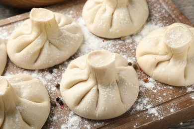 Photo of Uncooked khinkalis (dumplings) with peppercorns on wooden board, closeup