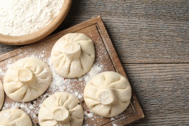 Photo of Uncooked khinkalis (dumplings) with peppercorns and flour on wooden table, flat lay. Space for text