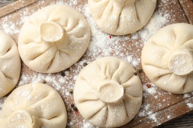 Photo of Uncooked khinkalis (dumplings) with peppercorns on wooden board, top view