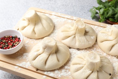 Photo of Uncooked khinkalis (dumplings), peppercorns and parsley on light table, closeup