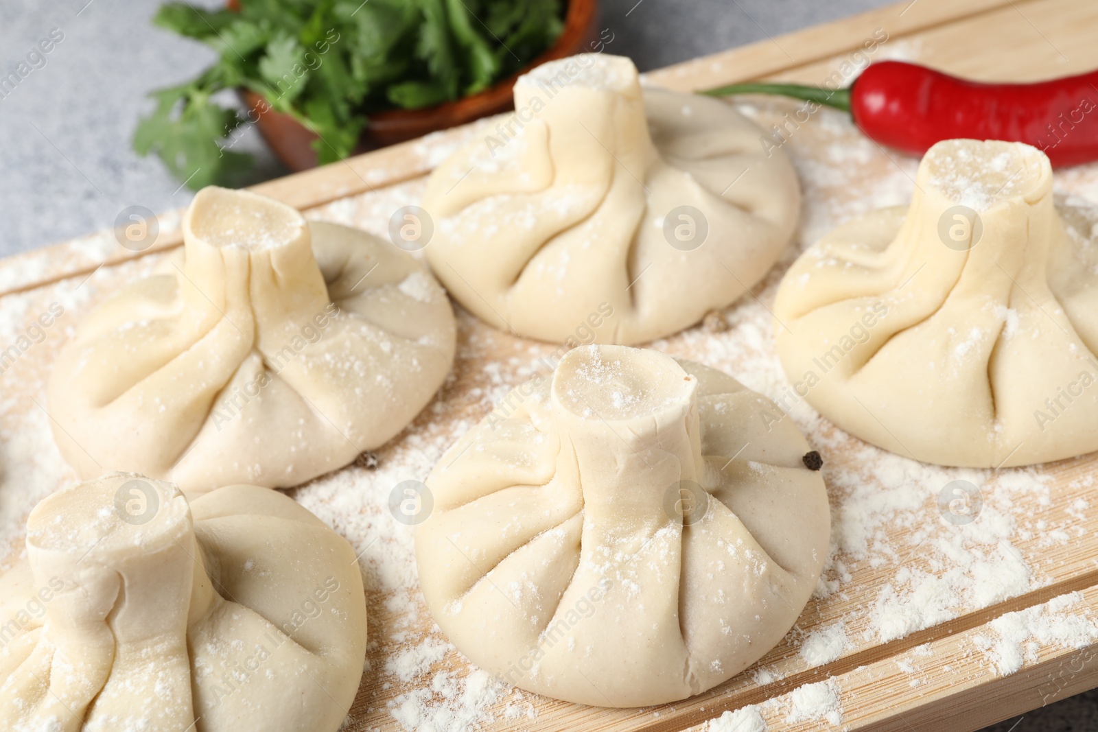 Photo of Uncooked khinkalis (dumplings), chili pepper and parsley on table, closeup