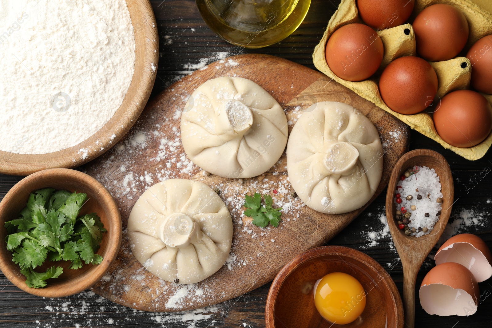 Photo of Uncooked khinkalis (dumplings) surrounded by ingredients on wooden table, flat lay