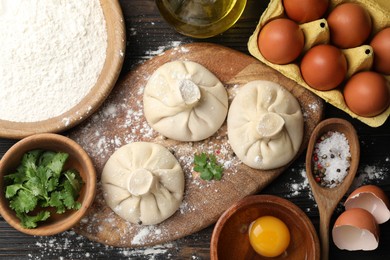 Photo of Uncooked khinkalis (dumplings) surrounded by ingredients on wooden table, flat lay