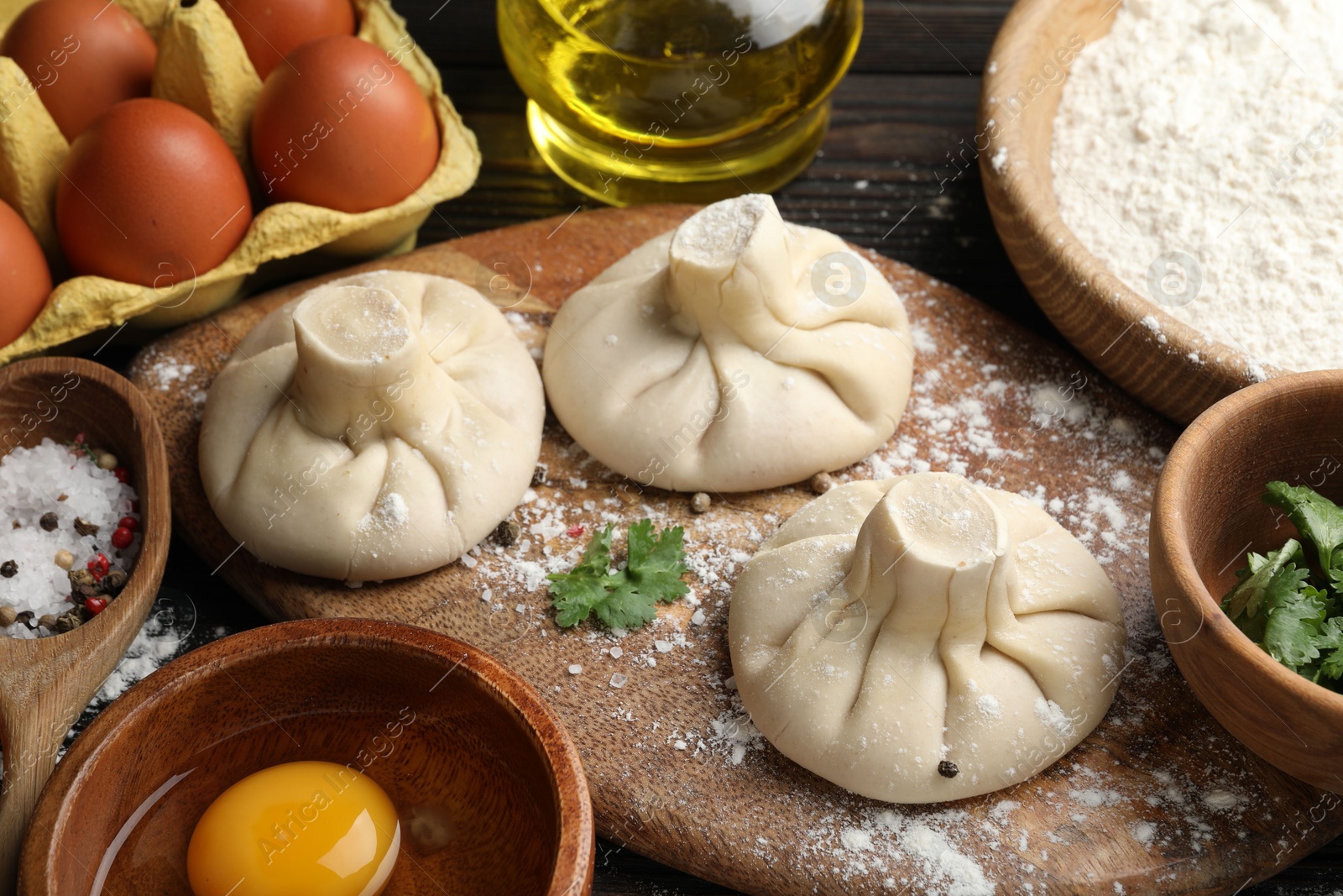 Uncooked khinkalis (dumplings) surrounded by ingredients on wooden table, closeup Photo of Uncooked khinkalis (dumplings) surrounded by ingredients on wooden table, closeup