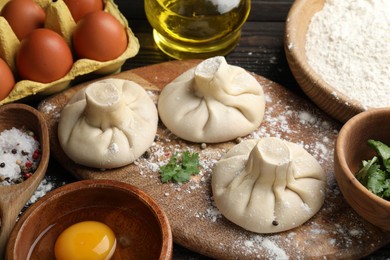 Photo of Uncooked khinkalis (dumplings) surrounded by ingredients on wooden table, closeup