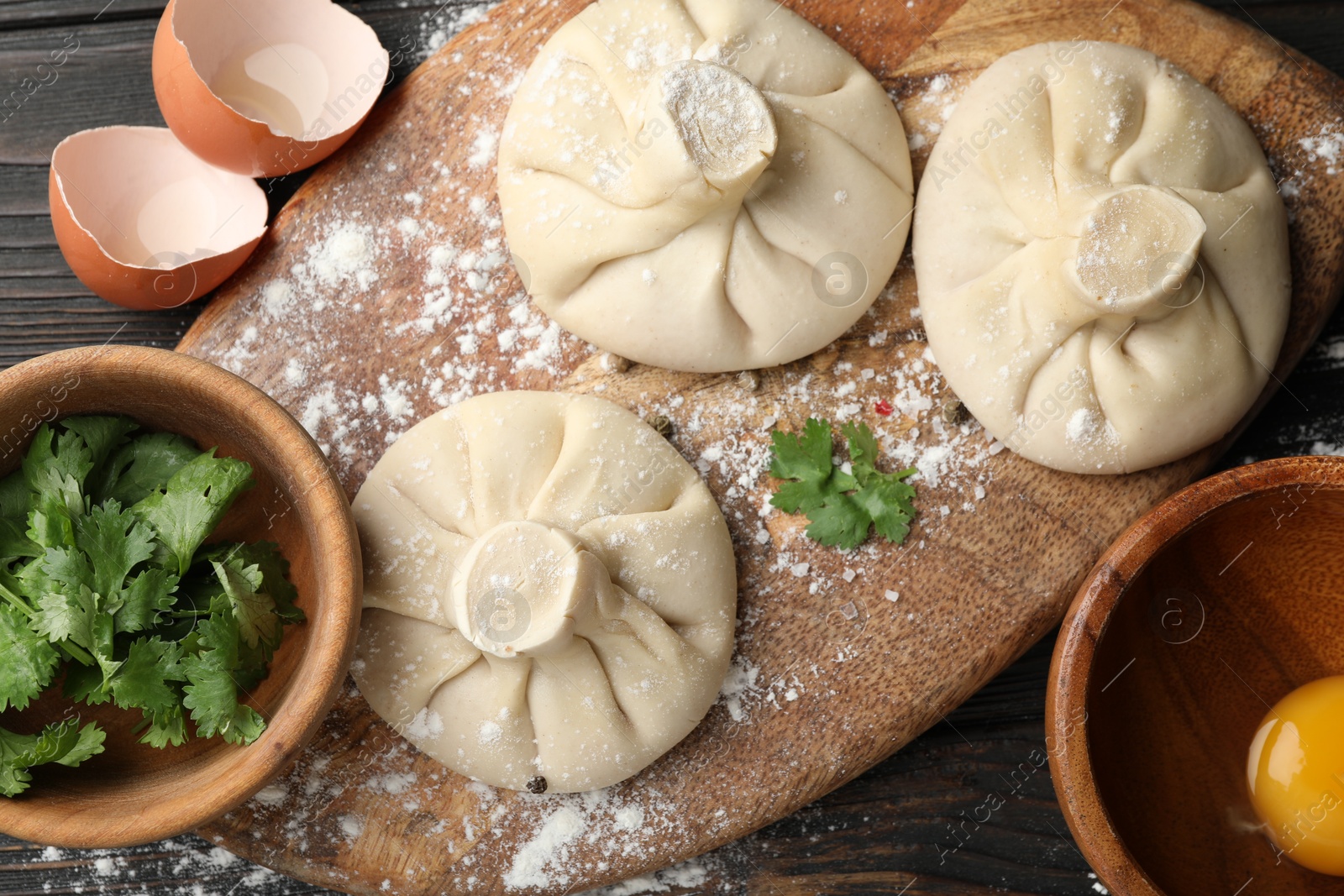 Photo of Uncooked khinkalis (dumplings) and ingredients on dark wooden table, flat lay