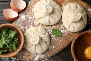 Photo of Uncooked khinkalis (dumplings) and ingredients on dark wooden table, flat lay