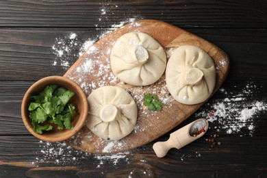 Photo of Uncooked khinkalis (dumplings), spices and parsley on dark wooden table, flat lay