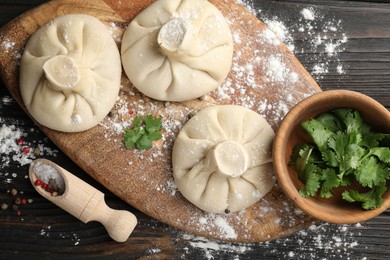 Photo of Uncooked khinkalis (dumplings), spices and parsley on dark wooden table, flat lay
