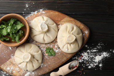 Photo of Uncooked khinkalis (dumplings), spices and parsley on dark wooden table, flat lay