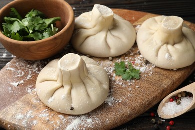 Photo of Uncooked khinkalis (dumplings), spices and parsley on wooden table, closeup