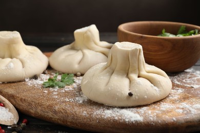 Photo of Uncooked khinkalis (dumplings), spices and parsley on wooden board, closeup