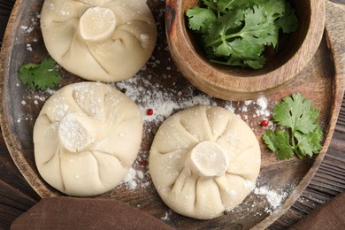 Photo of Uncooked khinkalis (dumplings) with peppercorns and parsley on wooden table, top view