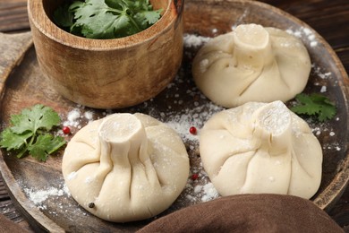 Photo of Uncooked khinkalis (dumplings) with peppercorns and parsley on wooden table, closeup