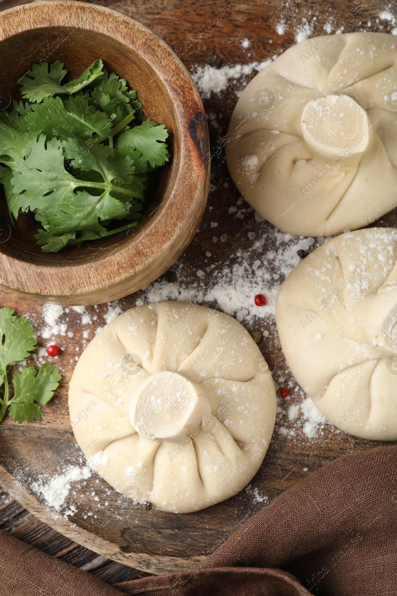 Uncooked khinkalis (dumplings) with peppercorns and parsley on wooden table, top view Photo of Uncooked khinkalis (dumplings) with peppercorns and parsley on wooden table, top view