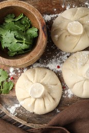 Photo of Uncooked khinkalis (dumplings) with peppercorns and parsley on wooden table, top view