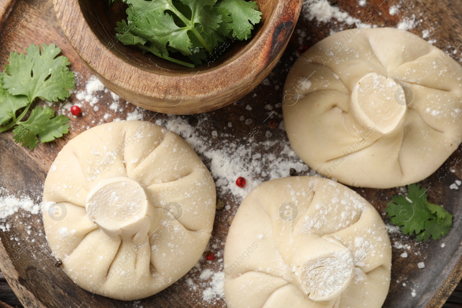 Photo of Uncooked khinkalis (dumplings) with peppercorns and parsley on wooden table, top view