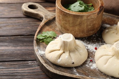 Photo of Uncooked khinkalis (dumplings) with peppercorns and parsley on wooden table, closeup