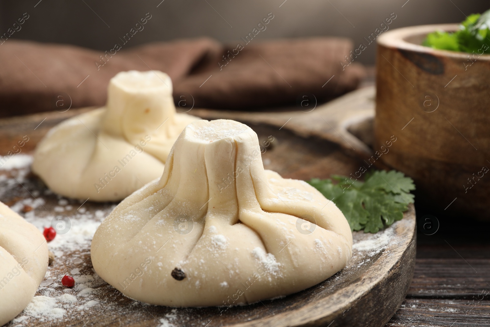 Photo of Uncooked khinkalis (dumplings) with peppercorns and parsley on wooden table, closeup