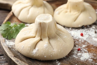 Photo of Uncooked khinkalis (dumplings) with peppercorns and parsley on wooden table, closeup