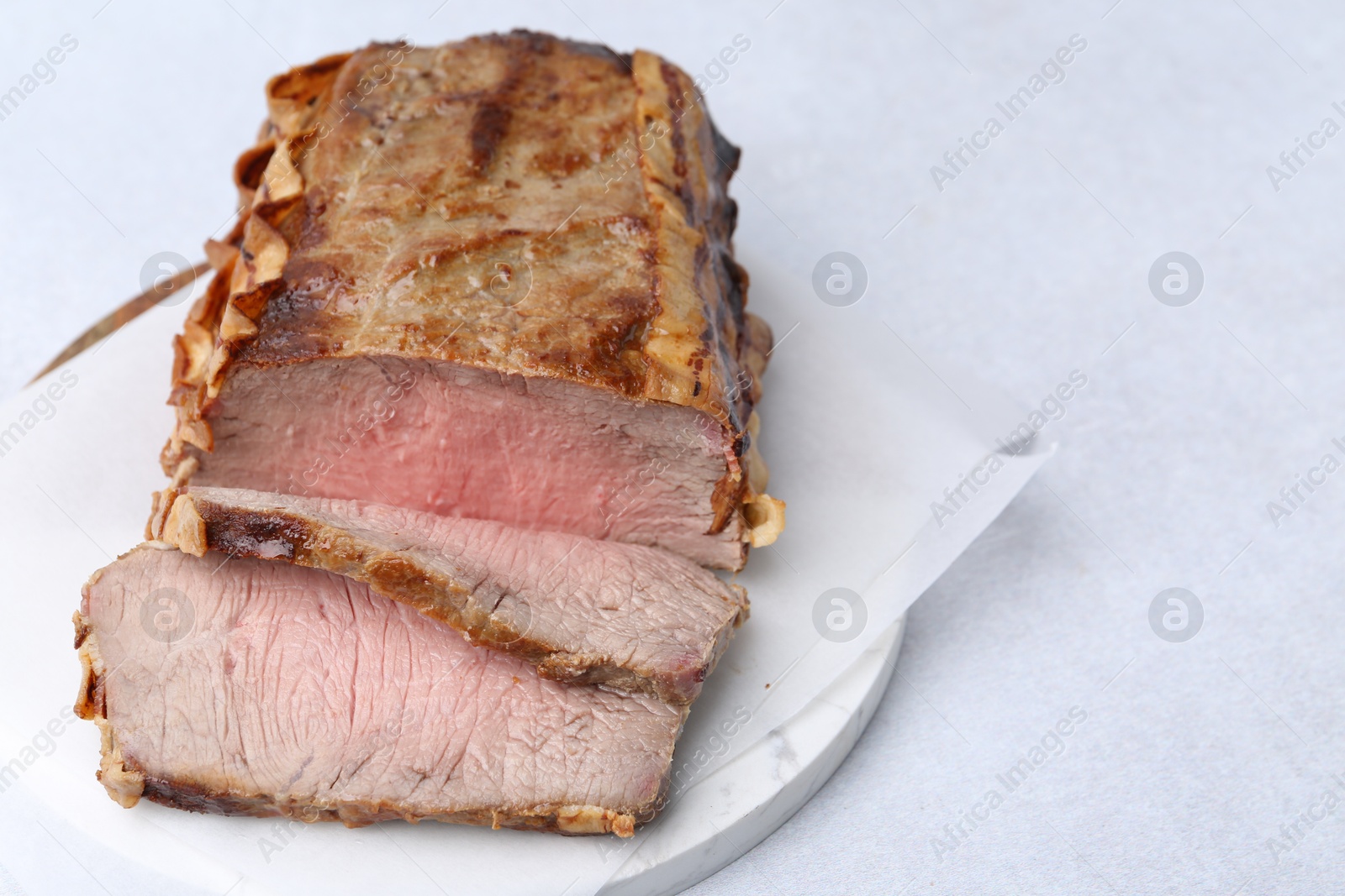 Photo of Delicious baked beef meat on light table, closeup. Space for text