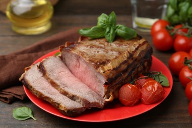 Photo of Delicious baked beef meat, tomatoes and basil on wooden table, closeup