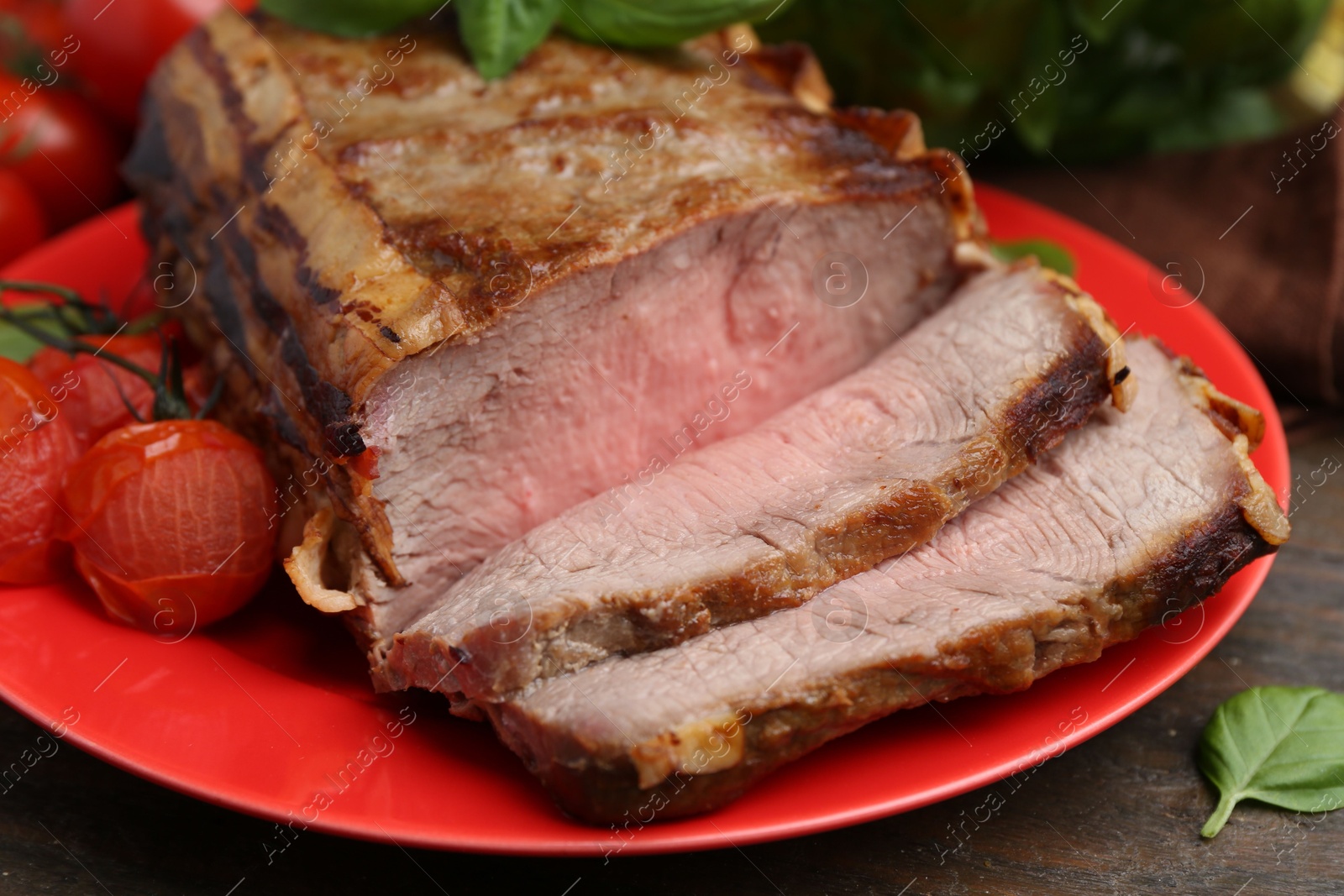 Photo of Delicious baked beef meat, tomatoes and basil on wooden table, closeup