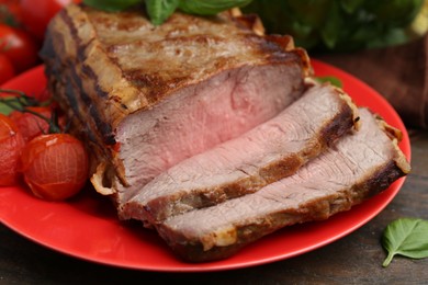 Photo of Delicious baked beef meat, tomatoes and basil on wooden table, closeup