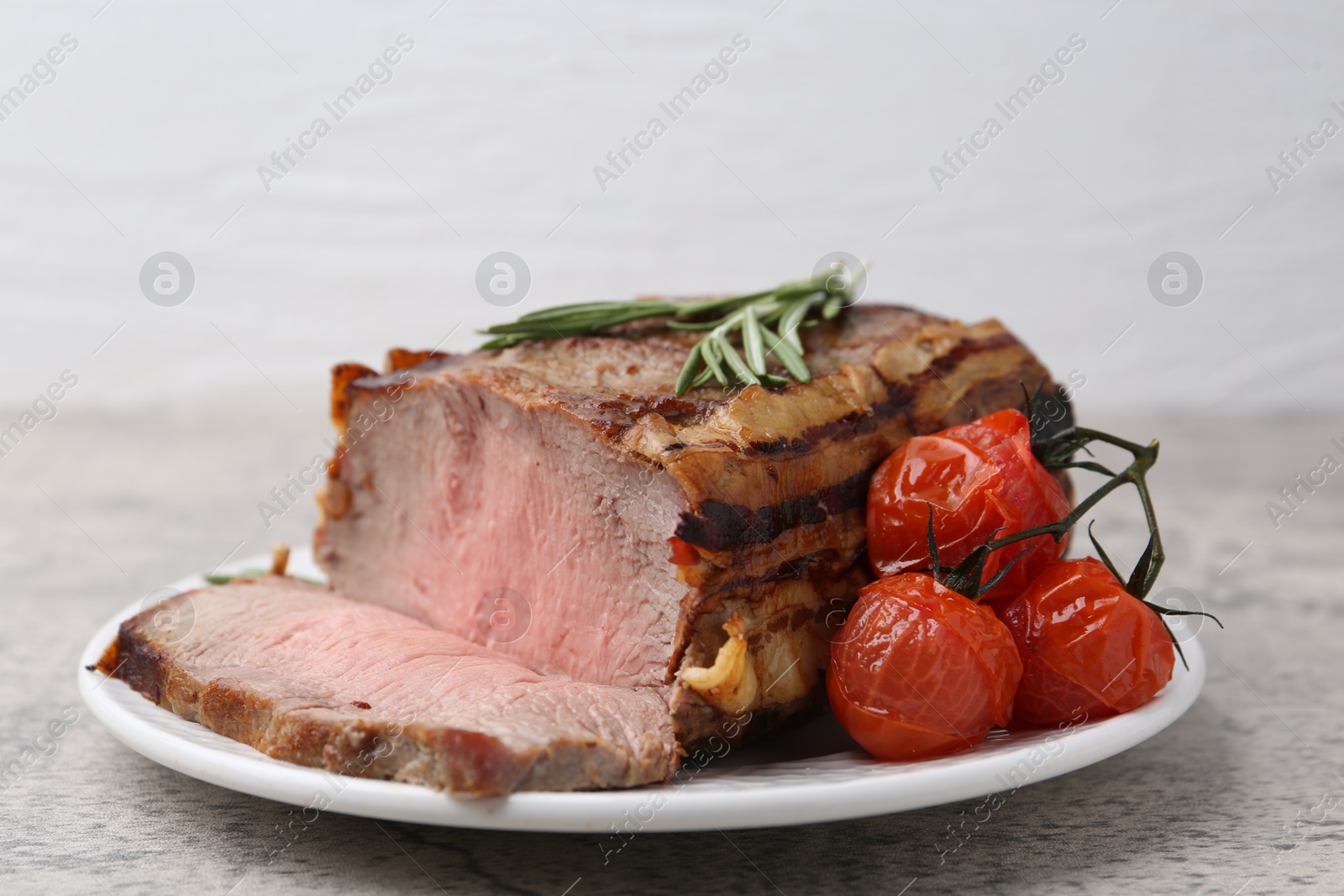 Photo of Delicious baked beef meat, tomatoes and rosemary on grey table, closeup