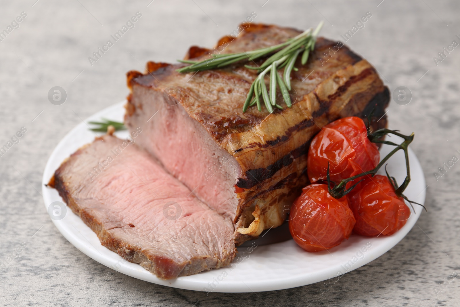 Delicious baked beef meat, tomatoes and rosemary on grey table, closeup Photo of Delicious baked beef meat, tomatoes and rosemary on grey table, closeup
