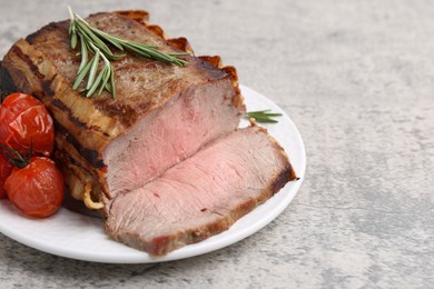 Photo of Delicious baked beef meat, tomatoes and rosemary on grey table, closeup. Space for text