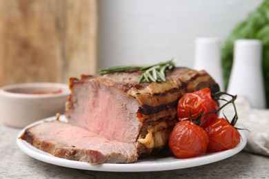 Photo of Delicious baked beef meat, tomatoes, rosemary and sauce on grey table, closeup