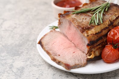 Photo of Delicious baked beef meat, tomatoes, rosemary and sauce on grey table, closeup. Space for text