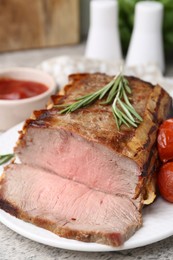 Photo of Delicious baked beef meat, tomatoes, rosemary and sauce on table, closeup
