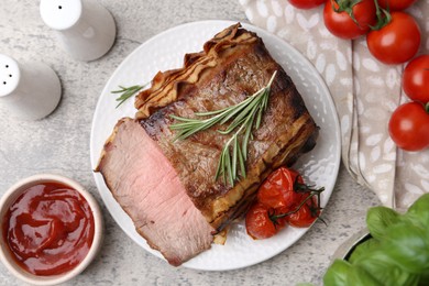 Photo of Delicious baked beef meat, tomatoes, basil, rosemary and sauce on grey table, flat lay