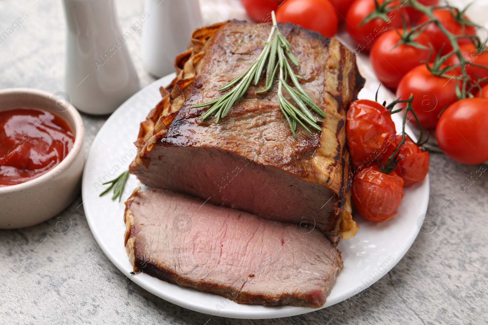 Delicious baked beef meat, tomatoes, rosemary and sauce on grey table, closeup Photo of Delicious baked beef meat, tomatoes, rosemary and sauce on grey table, closeup