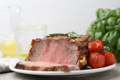 Photo of Delicious baked beef meat, tomatoes, rosemary and basil on grey table, closeup