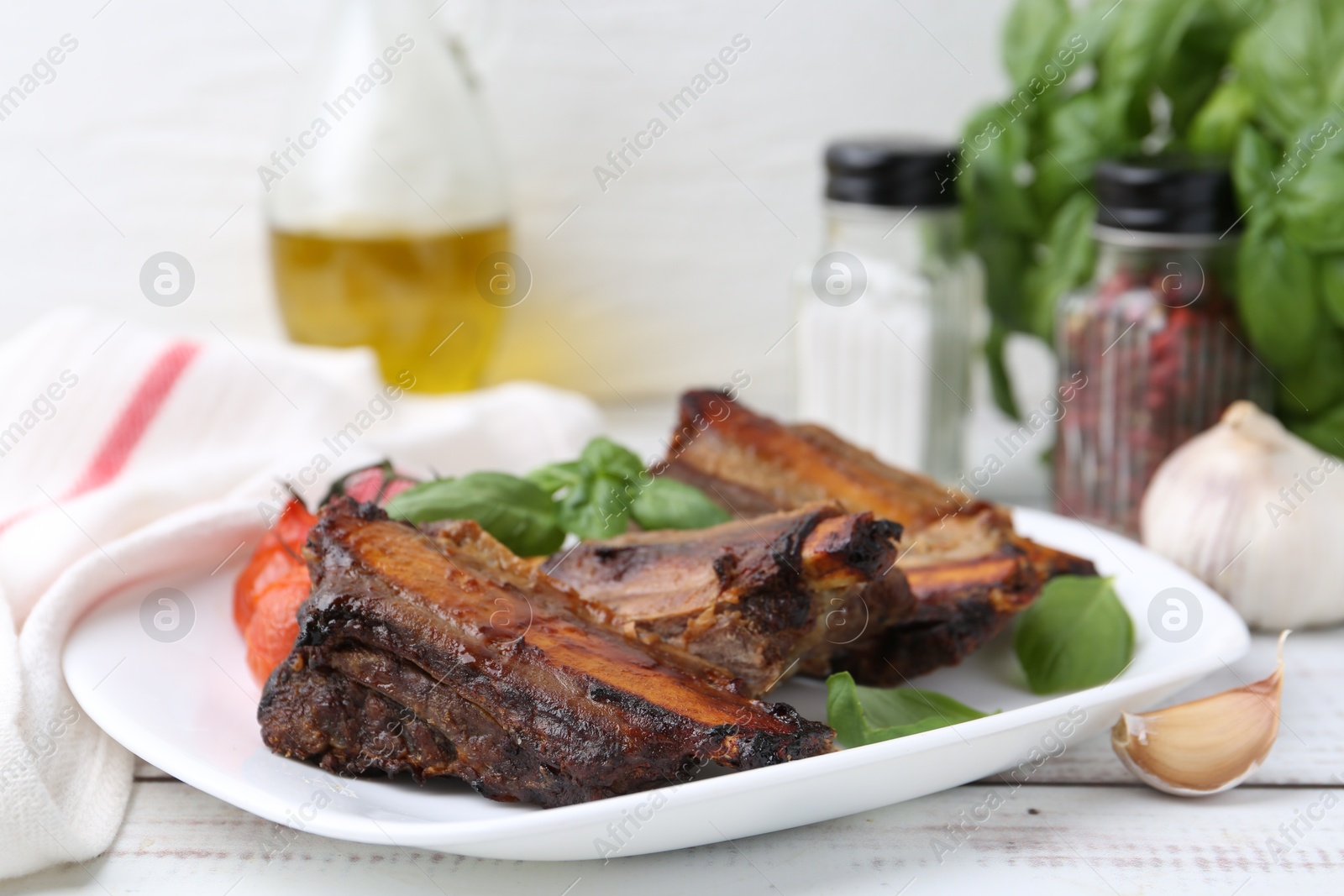 Roasted beef ribs, tomatoes and spices on white wooden table, closeup Photo of Roasted beef ribs, tomatoes and spices on white wooden table, closeup