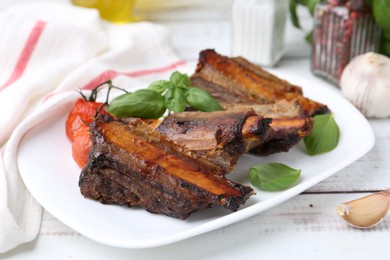 Photo of Roasted beef ribs, tomatoes and spices on white wooden table, closeup