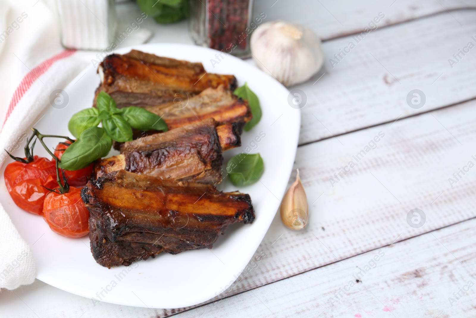 Roasted beef ribs, tomatoes and spices on white wooden table, closeup. Space for text Photo of Roasted beef ribs, tomatoes and spices on white wooden table, closeup. Space for text