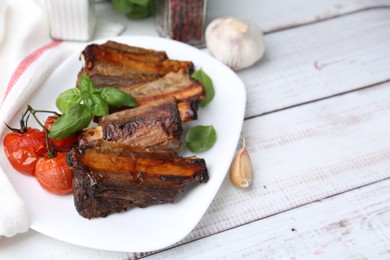 Photo of Roasted beef ribs, tomatoes and spices on white wooden table, closeup. Space for text