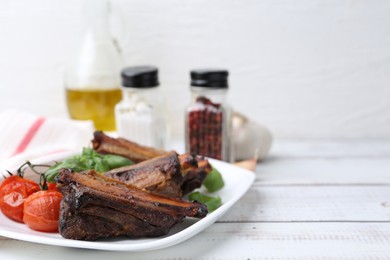 Photo of Roasted beef ribs, tomatoes and spices on white wooden table, closeup. Space for text