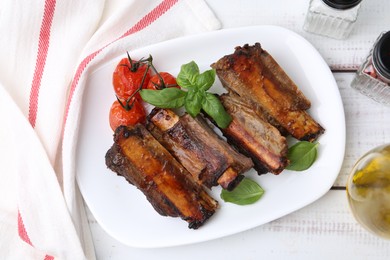 Photo of Roasted beef ribs, tomatoes and spices on white wooden table, flat lay