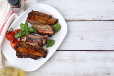 Photo of Roasted beef ribs, tomatoes and spices on white wooden table, flat lay. Space for text